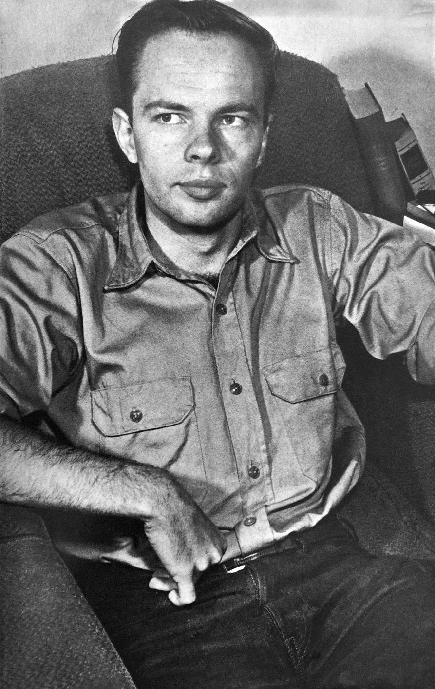 A black-and-white portrait photograph of the young science-fiction writer Philip K. Dick in the early 1960s, seated in an armchair in a work shirt, looking to one side