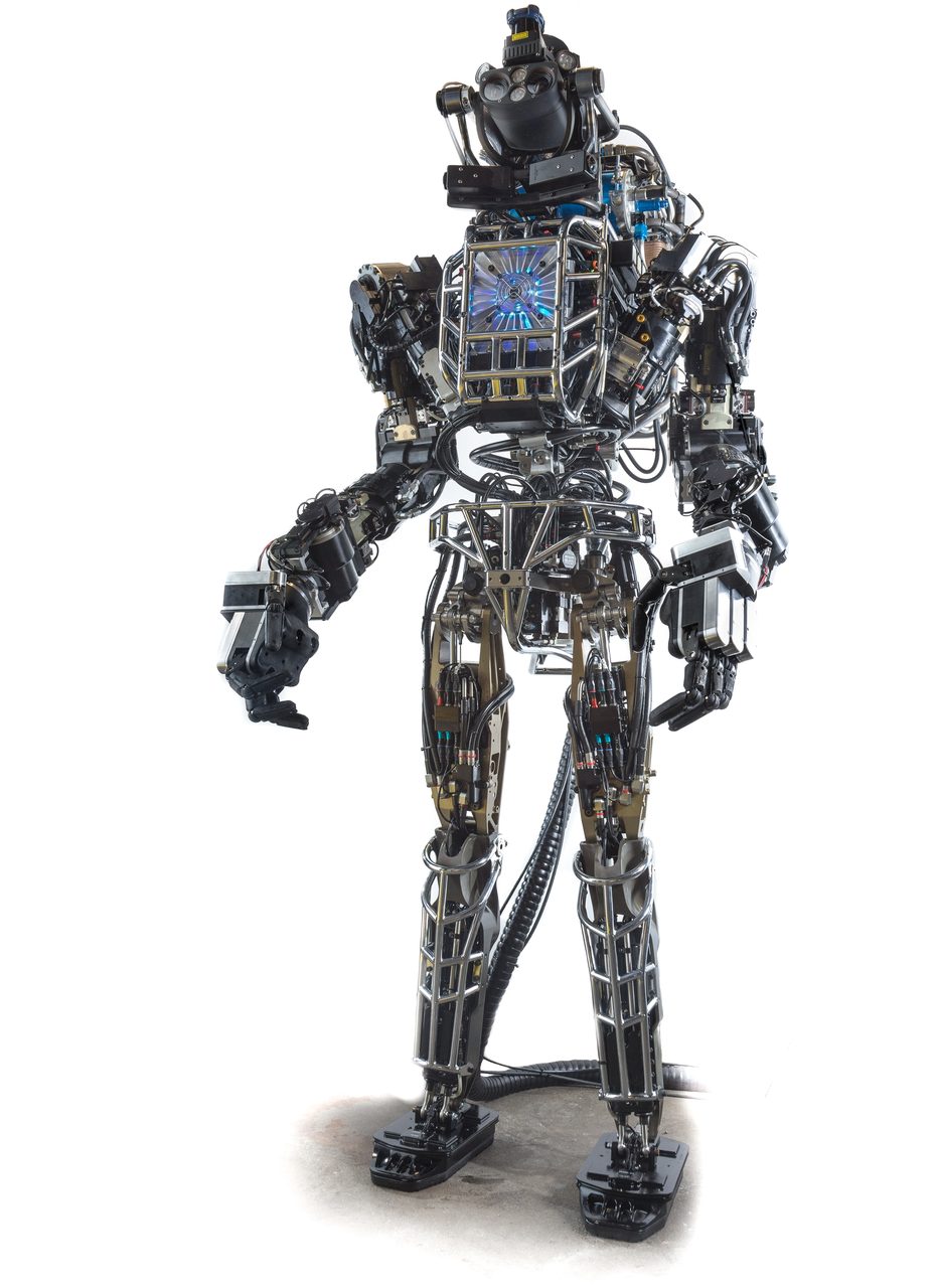 A front view of a tall humanoid robot standing against a plain seamless backdrop, its limbs and torso built around exposed hydraulic hardware