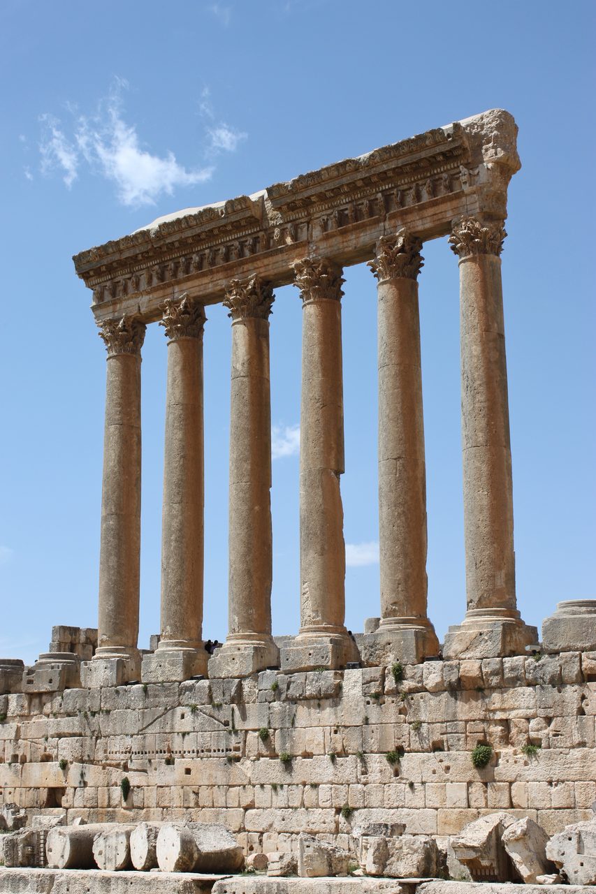Six tall columns of the Temple of Jupiter at Baalbek still standing on their podium, with deeply carved foliate capitals and a surviving section of entablature above them