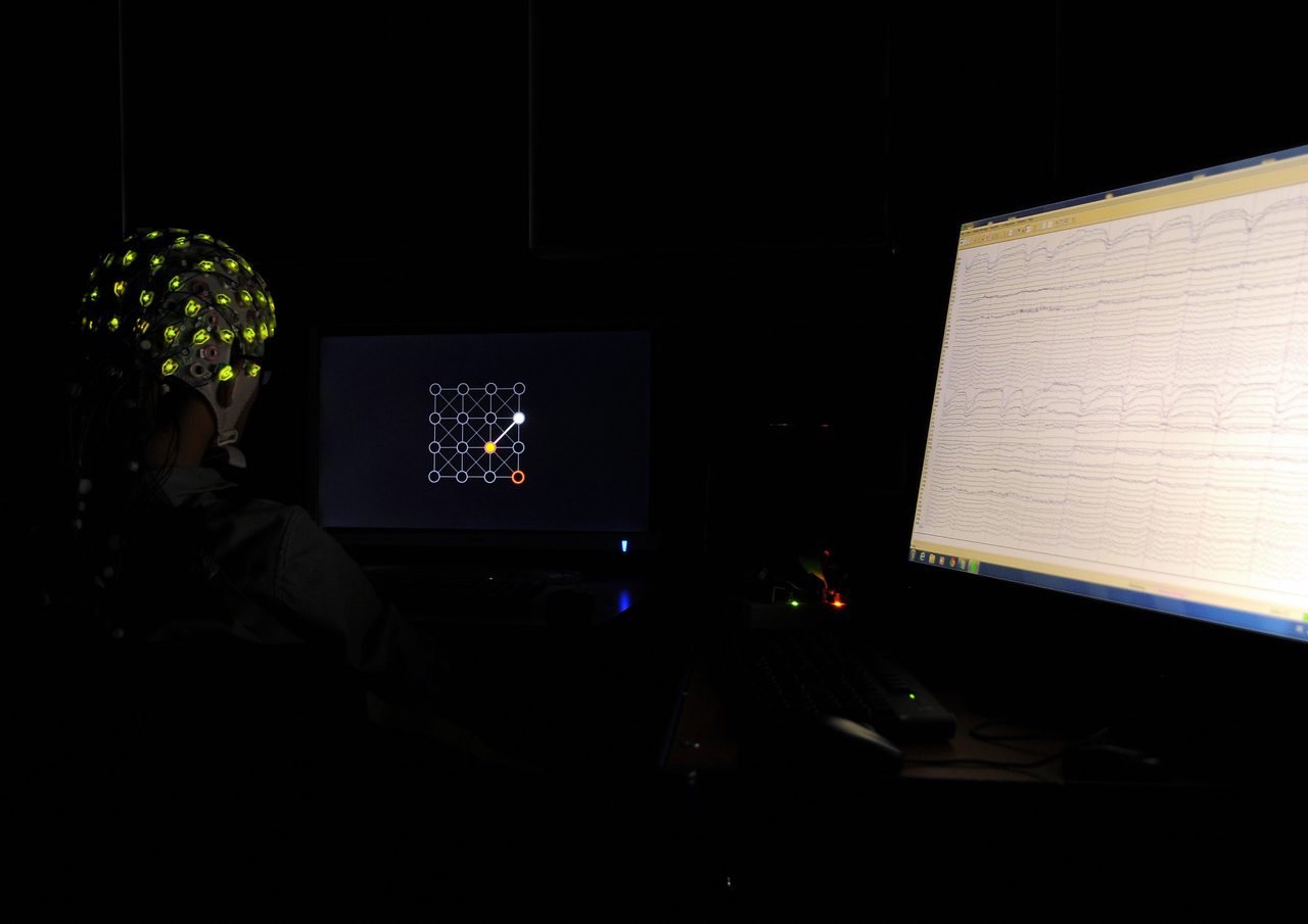 A participant wearing an EEG electrode cap, with recorded brain activity displayed and used to steer a cursor on a screen