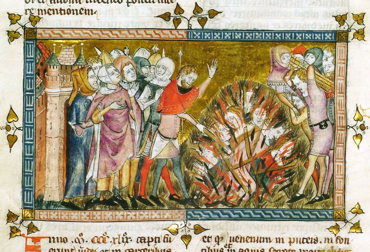 A medieval manuscript page: within a painted border, an armed crowd stands beside a masonry town tower at the left while at the right human figures burn inside a heap of blazing brushwood and men in short tunics carry more bundles of wood to the fire; lines of Latin in a gothic hand run above and below the picture