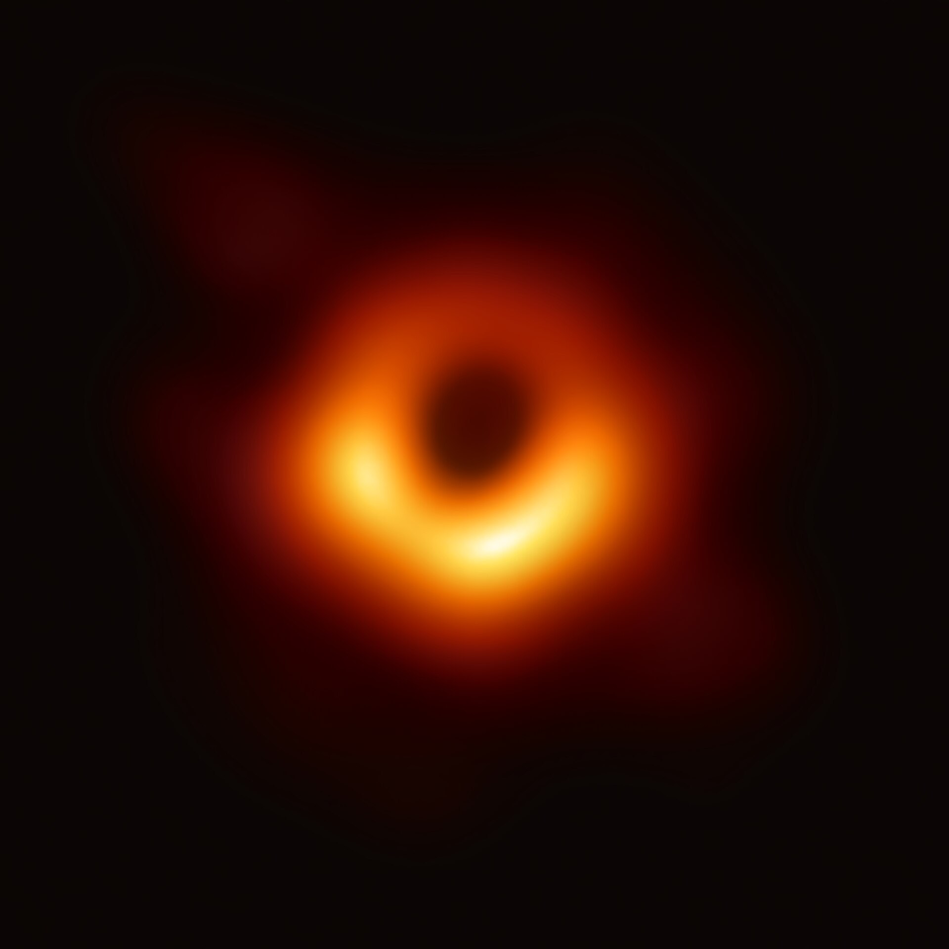 The first Event Horizon Telescope image of a black hole: a bright, asymmetric orange-gold ring of light, brighter along its lower edge, surrounding a dark central shadow, against a black background