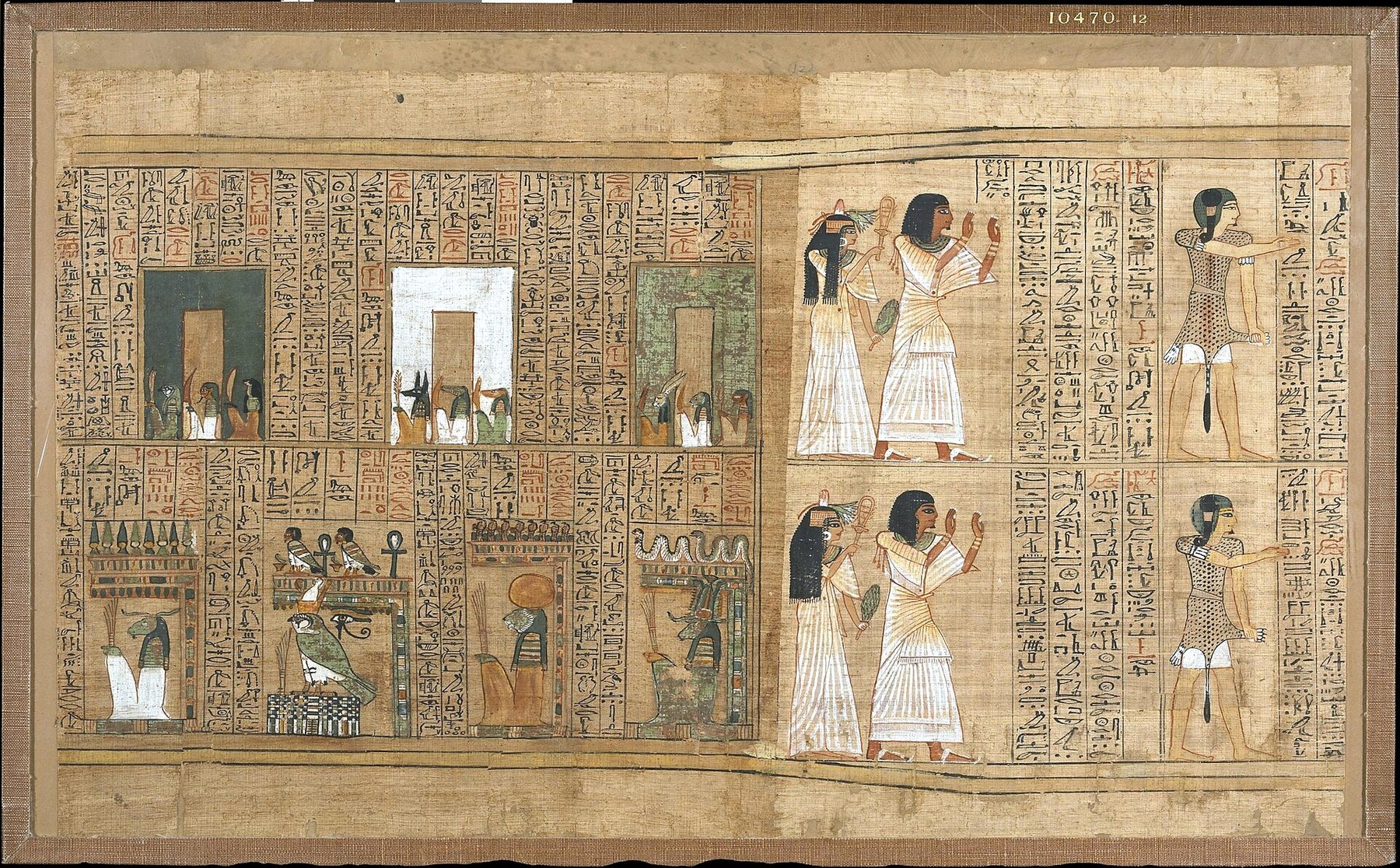 A mounted papyrus sheet on a fabric backing with the accession number 10470.12 printed at the top right. The sheet is dominated by dense columns of hieroglyphs in black with red rubrics. At the left are three coloured rectangular panels, dark grey-blue, white and green, each containing a doorway shape, with small groups of seated deities beneath them including jackal-headed, falcon-headed and ram-headed figures. Lower left are shrines and standards, a falcon on a plinth with a wedjat eye, ankh signs and a serpent motif. At the right, two registers each show a woman in a pleated white gown holding a sistrum and a man in pleated linen with hands raised, and beside them a figure in a spotted garment with arms outstretched.
