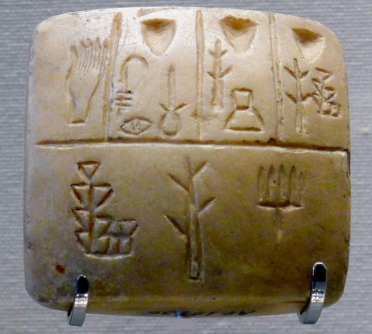 A small squarish clay tablet lit from one side, its face covered with impressed proto-cuneiform signs.
