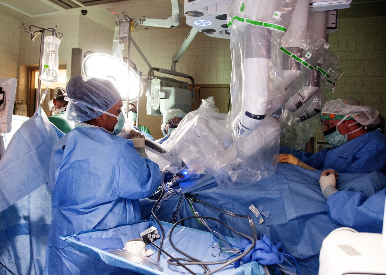 Medical personnel in an operating theatre working with a multi-armed robotic surgical system positioned over a patient