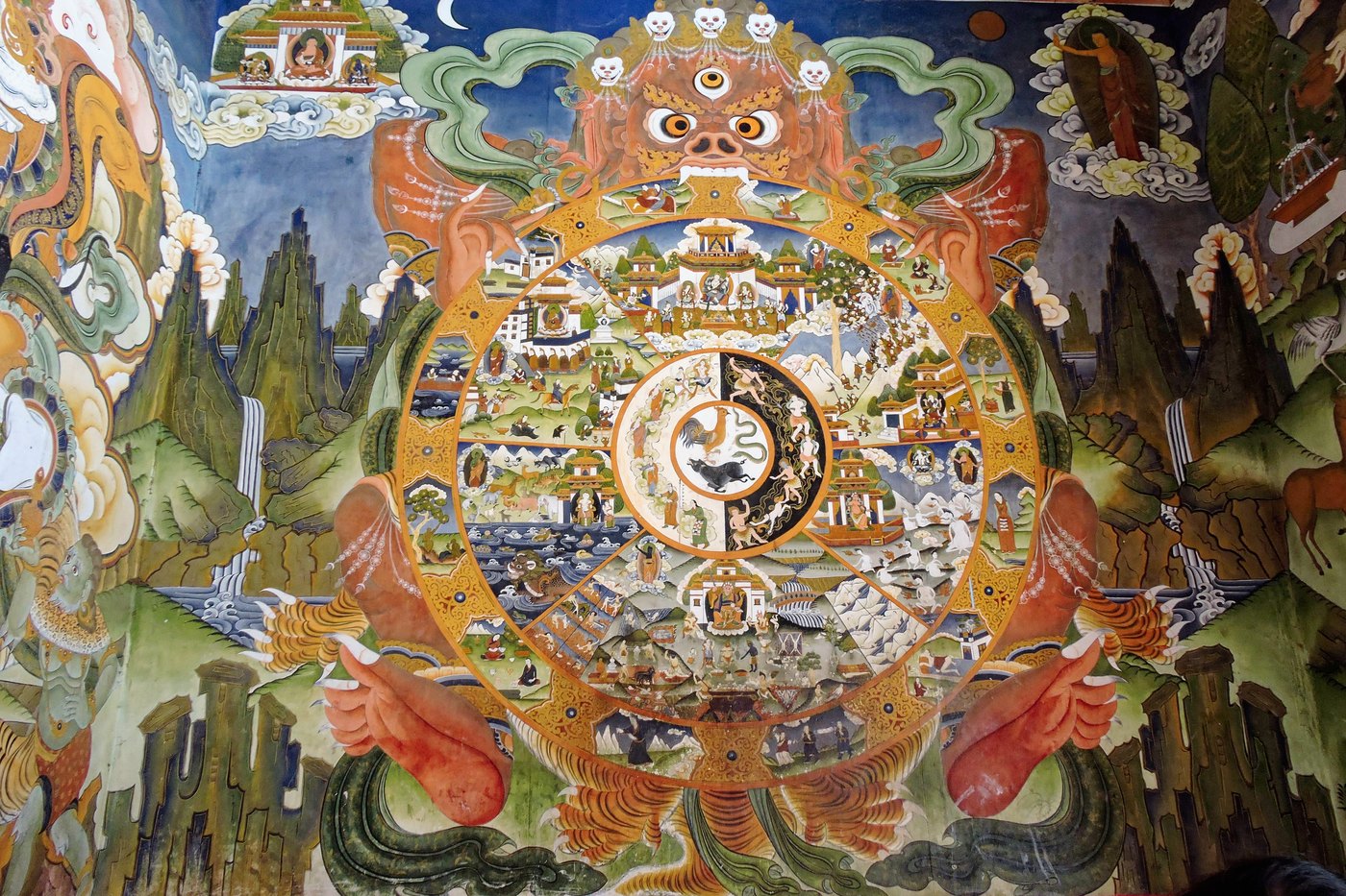 A Tibetan Buddhist Wheel of Life (bhavachakra) mural, showing the six realms of rebirth arranged in a great wheel held in the jaws of a fearsome figure