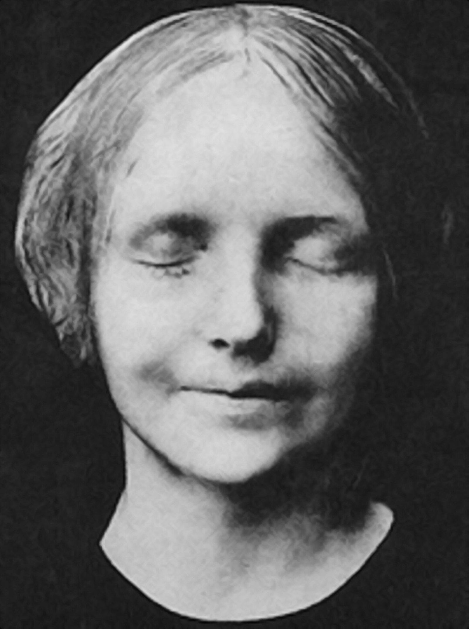 An old black and white photograph of a plaster mask of a young woman's face against a black ground. The eyes are closed, the mouth is closed with the faintest upward curve at one corner, and the hair is parted in the middle and drawn back smoothly. The plaster is lit from the left and the surface is slightly grainy. The mask ends in a curved edge below the chin.
