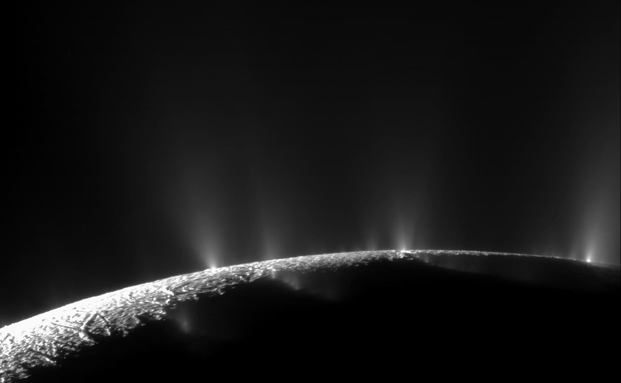 Saturn's moon Enceladus backlit by the sun, showing distinct jets of icy spray erupting from fractures near its south pole