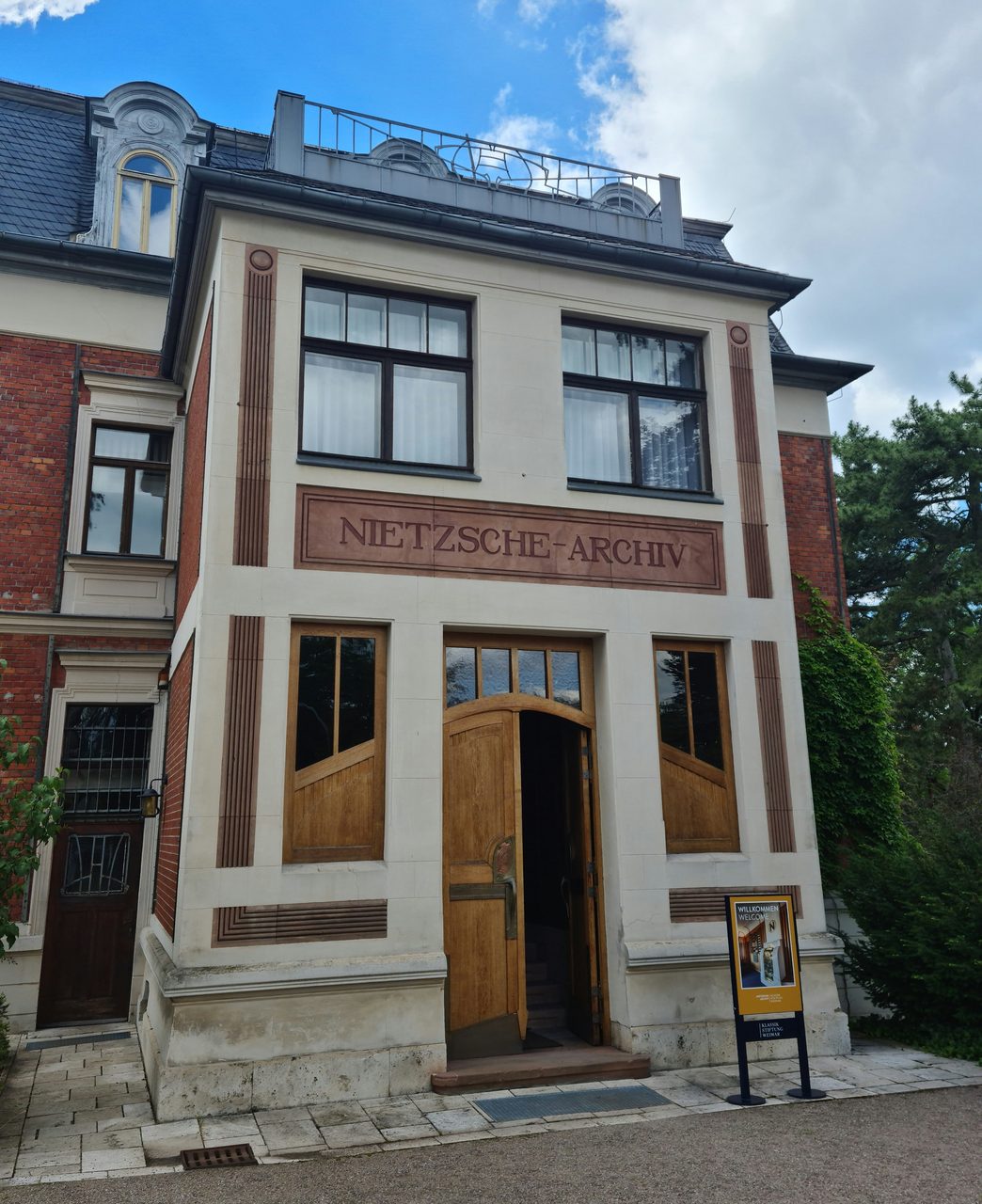 The entrance of the Nietzsche-Archiv in Weimar, its name cut in capitals above an open door, with a visitor sign on the path