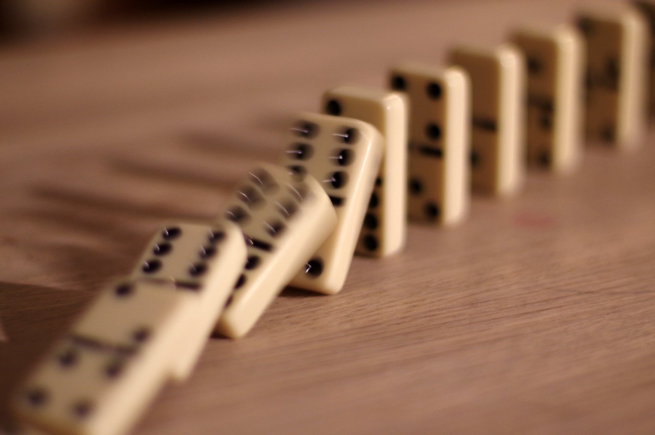 A line of dominoes caught mid-fall, each toppling the next in sequence