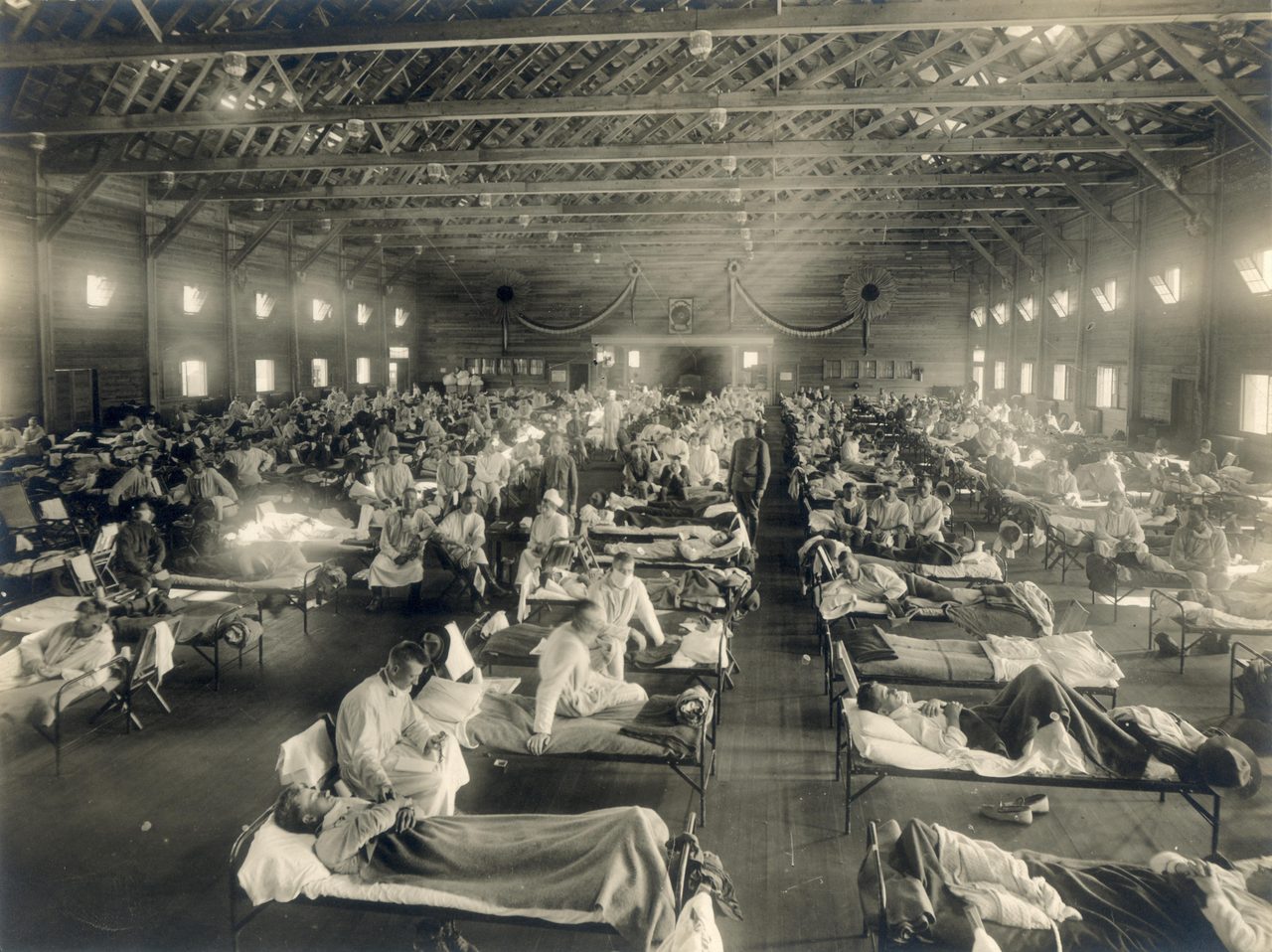 A wide interior photograph of rows of beds holding patients in a large emergency hospital ward during the 1918 influenza epidemic