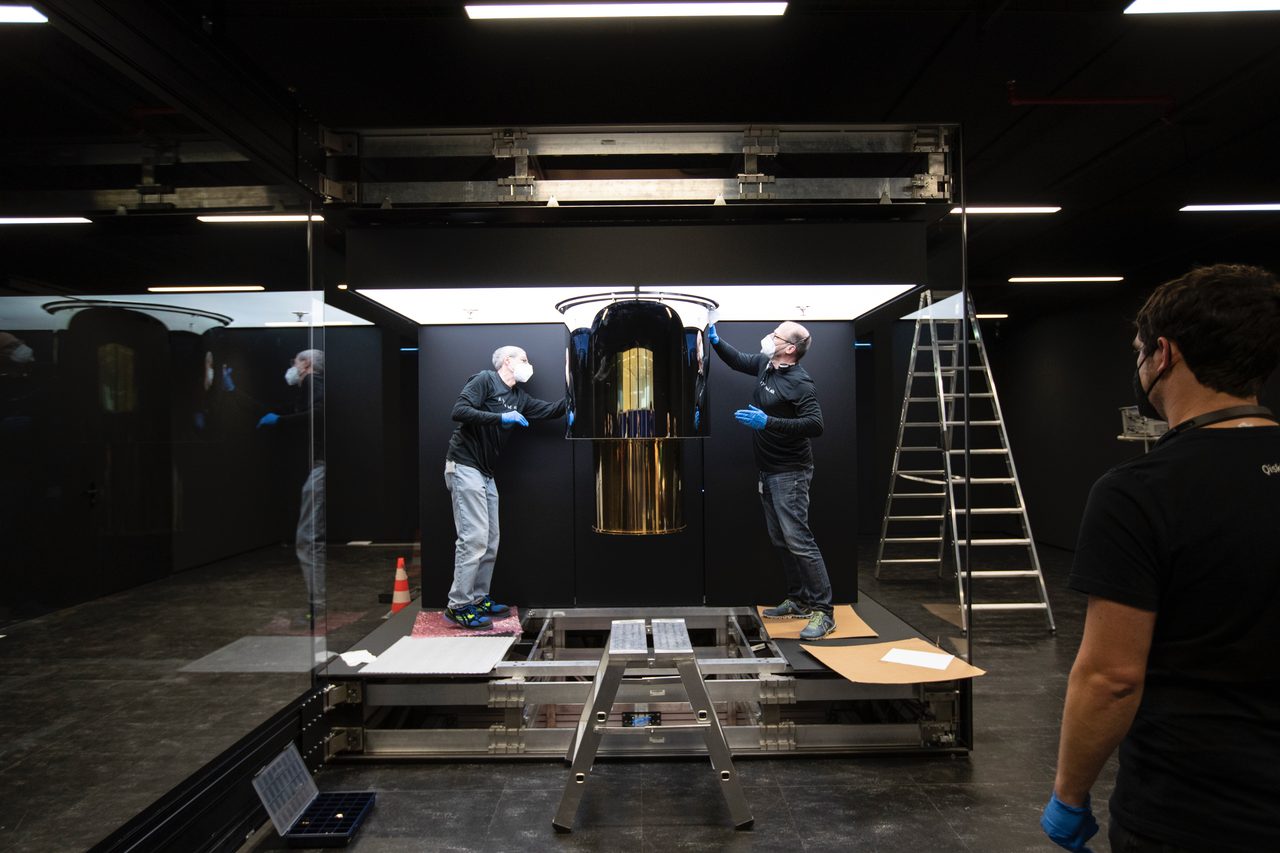 Engineers installing an IBM Quantum System One, a gold cylindrical cryostat inside a black glass enclosure