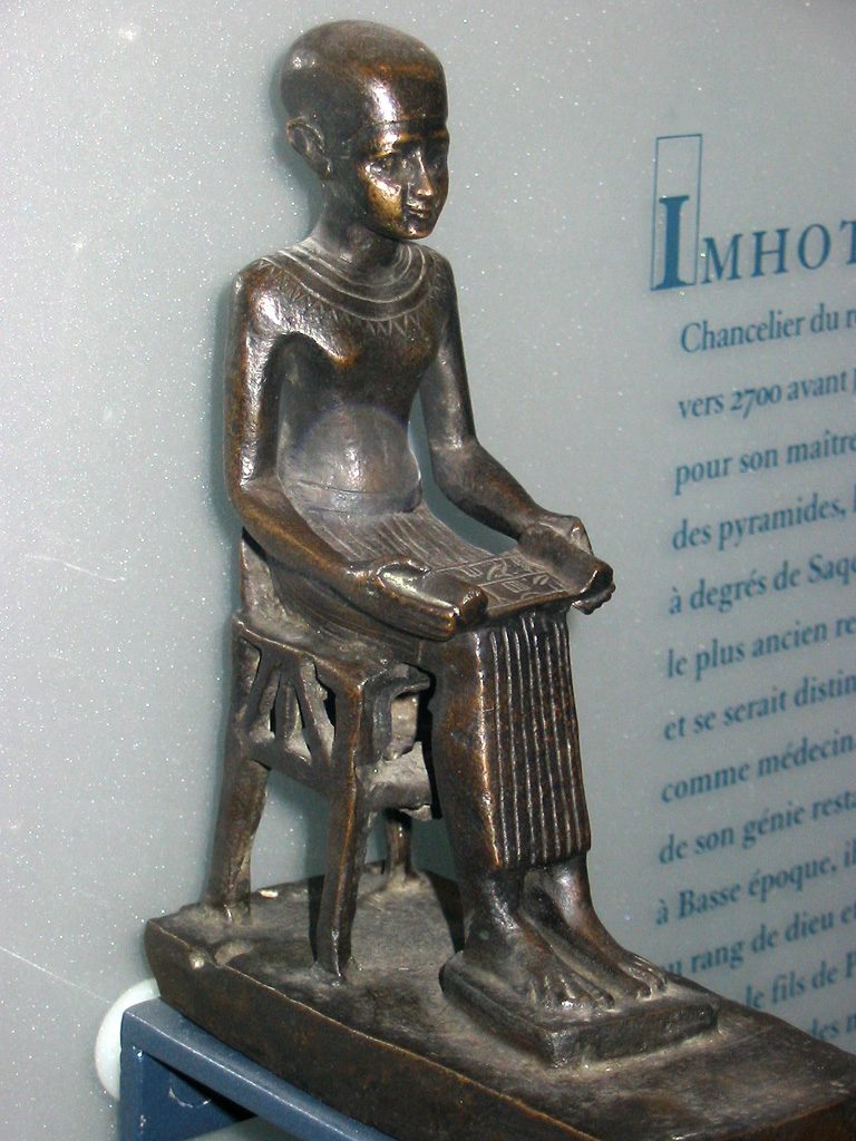 A small bronze statuette of a seated figure holding an unrolled papyrus scroll on his lap