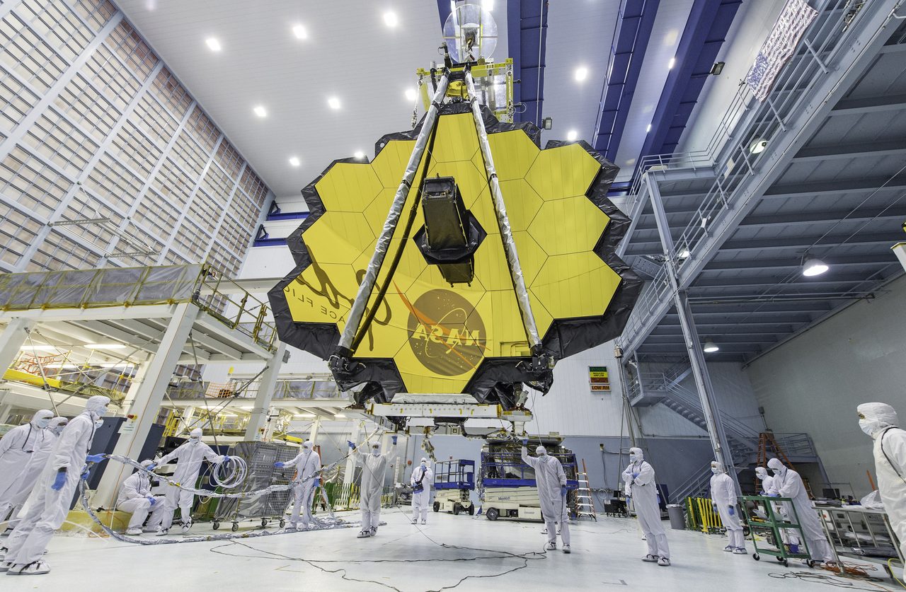 NASA technicians lifting the fully deployed 18-segment gold primary mirror of the James Webb Space Telescope inside a clean room