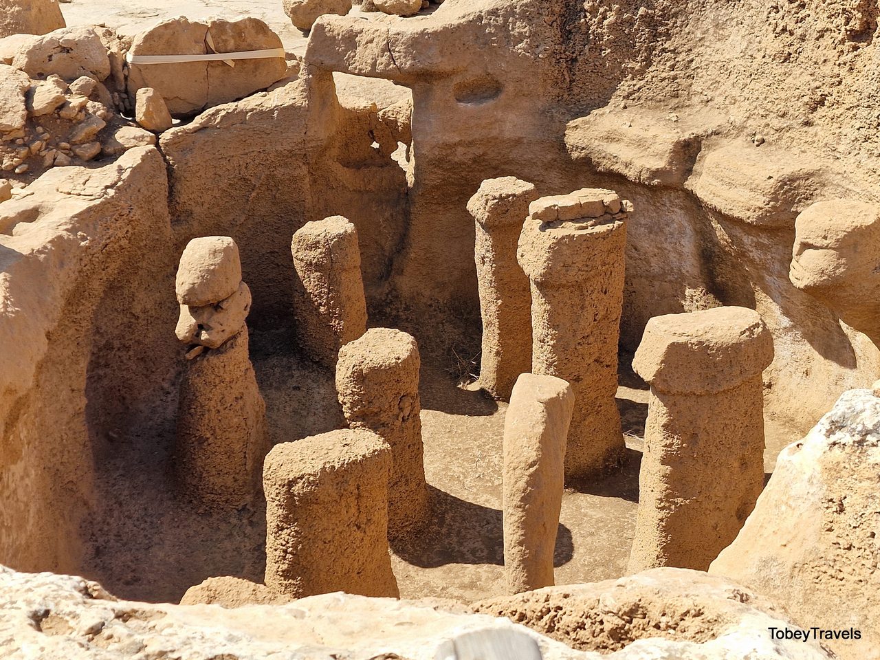 The bedrock-carved interior of Structure AB at Karahan Tepe, showing phallus-shaped pillars and a carved human head within the chamber