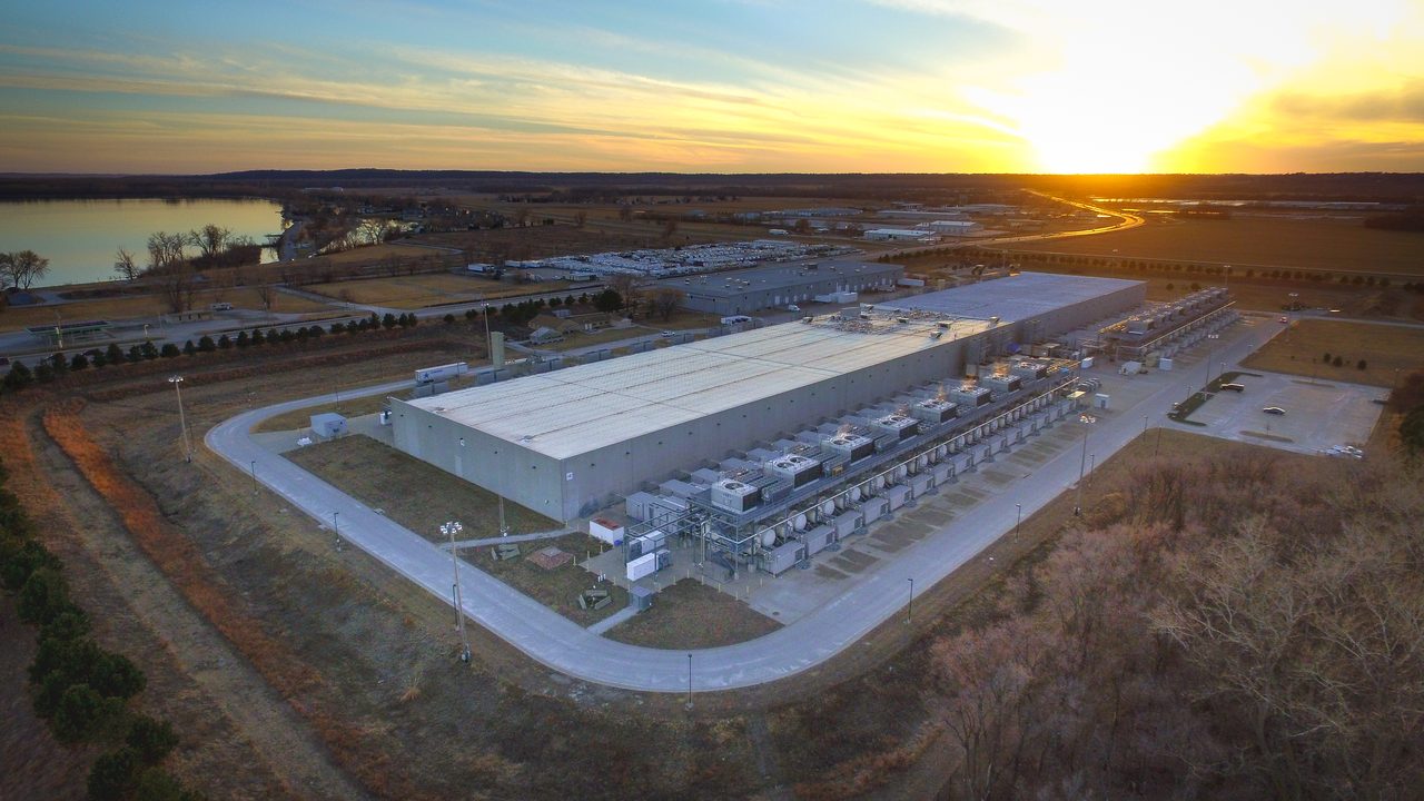 An aerial photograph of long, low, windowless buildings with pale roofs standing on flat open ground: the Google data centre at Council Bluffs, Iowa