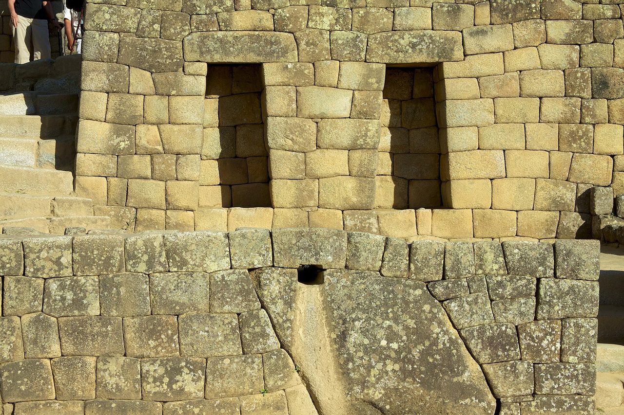 A carved stone water channel and spout at Machu Picchu, alongside two trapezoidal window openings