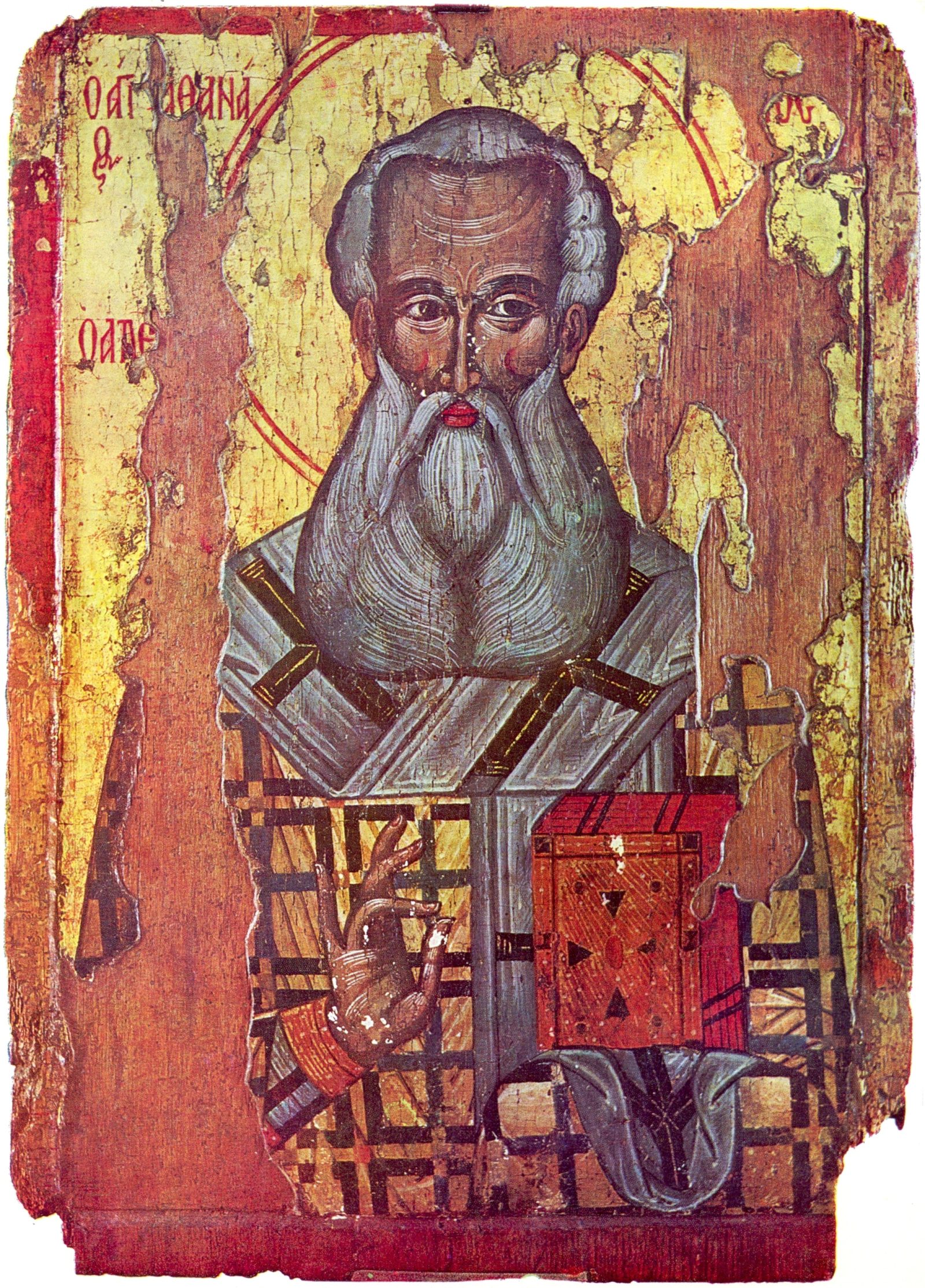 A worn painted panel. An elderly bearded bishop with a long white beard faces forward, wearing a pale grey vestment marked with dark crosses over red and gold. One hand is raised, and the other holds a red book decorated with dark triangles. The gold background has flaked away over much of the panel to bare reddish wood. Greek lettering in red appears at the upper left, and a red border frames the whole.