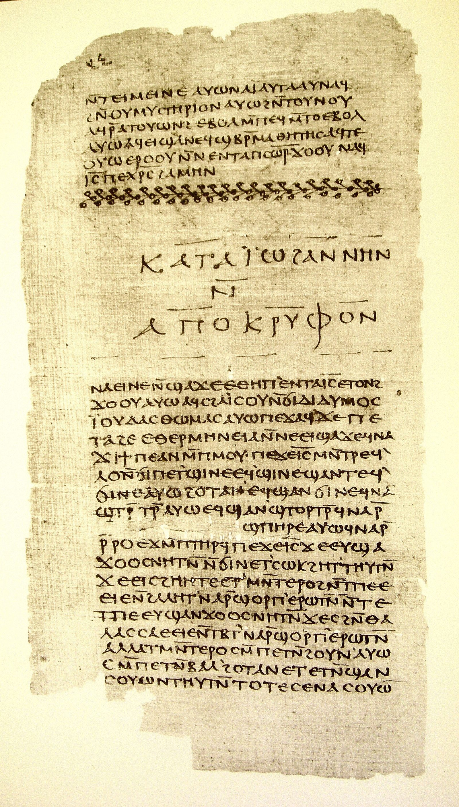A papyrus leaf photographed against a pale ground, torn along the top and bottom edges and fibrous at the margins. An upper block of about six lines of Coptic uncials ends in a short line. Below it runs a ruled band of looping chain ornament across the full width of the page. Below that, a title in much larger, widely spaced letters on three centred lines, ruled above and below. Then a second block of roughly nineteen lines in the same hand, running down to the torn lower edge.