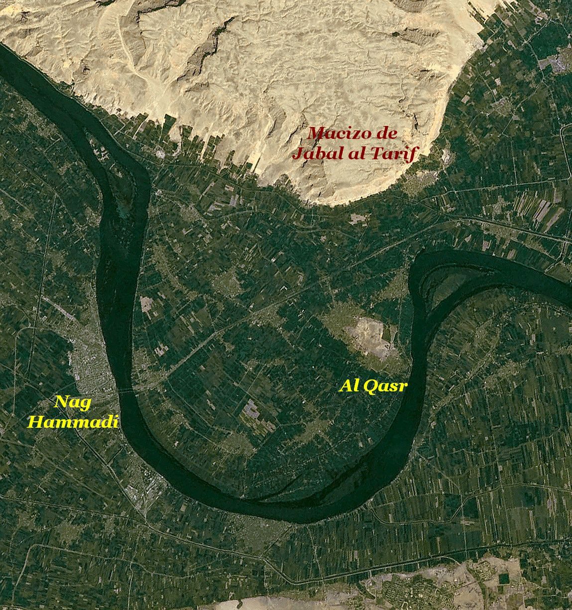 A satellite photograph. A great dark loop of the Nile winds through deep green cultivated floodplain across the lower two thirds of the frame. Pale bare desert and eroded cliffs occupy the top. Three labels are overlaid: one in red on the cliffs, and two in yellow, one at the lower left and one at the right.