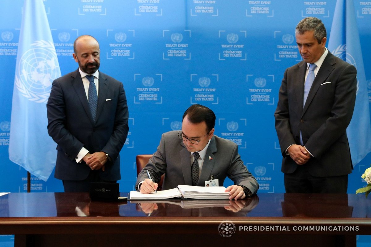 A diplomat in a suit seated at a United Nations desk signing a document, formally signing the Treaty on the Prohibition of Nuclear Weapons