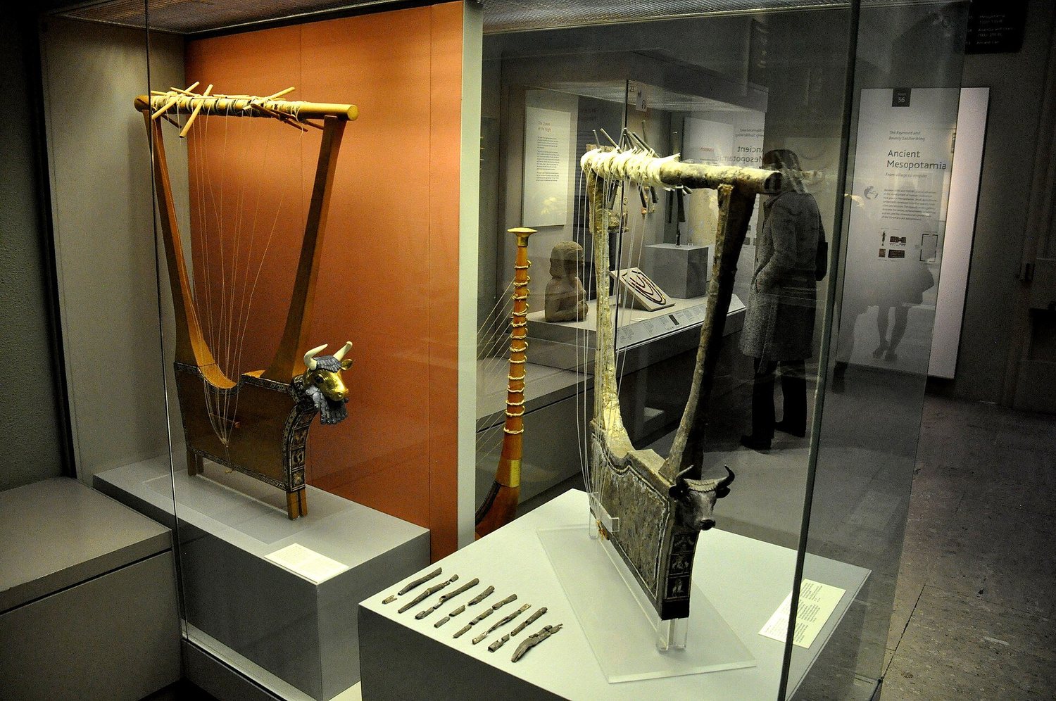Two reconstructed lyres in a glass museum case: the left with a golden bull's head at the front and strings running to a sound box, the right with a silver bull's head and frame, in a gallery labelled Ancient Mesopotamia
