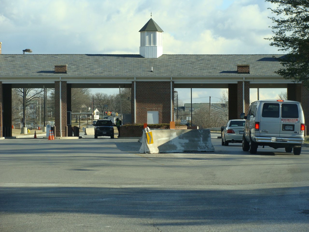A vehicle checkpoint gate at Fort George G. Meade, Maryland, with a brick guardhouse, a cupola, and concrete security barriers