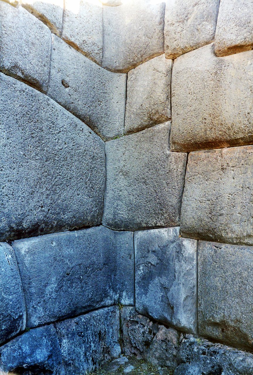 A close-up photograph of mortar-free polygonal joints at Sacsayhuaman, multi-sided stone faces fitted directly against one another with no visible gap