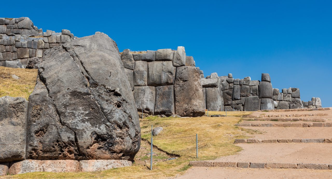 A row of precisely fitted stone corners along the zigzag walls of Sacsayhuaman, the outward and inward angles of the dry-stone construction visible along the run of the wall