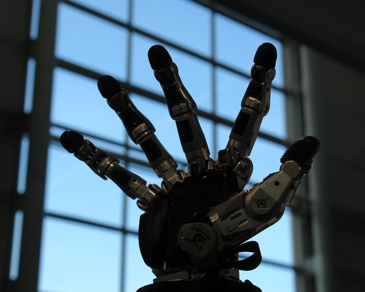 A metallic anthropomorphic robotic hand with its five fingers spread, exhibited at a trade fair