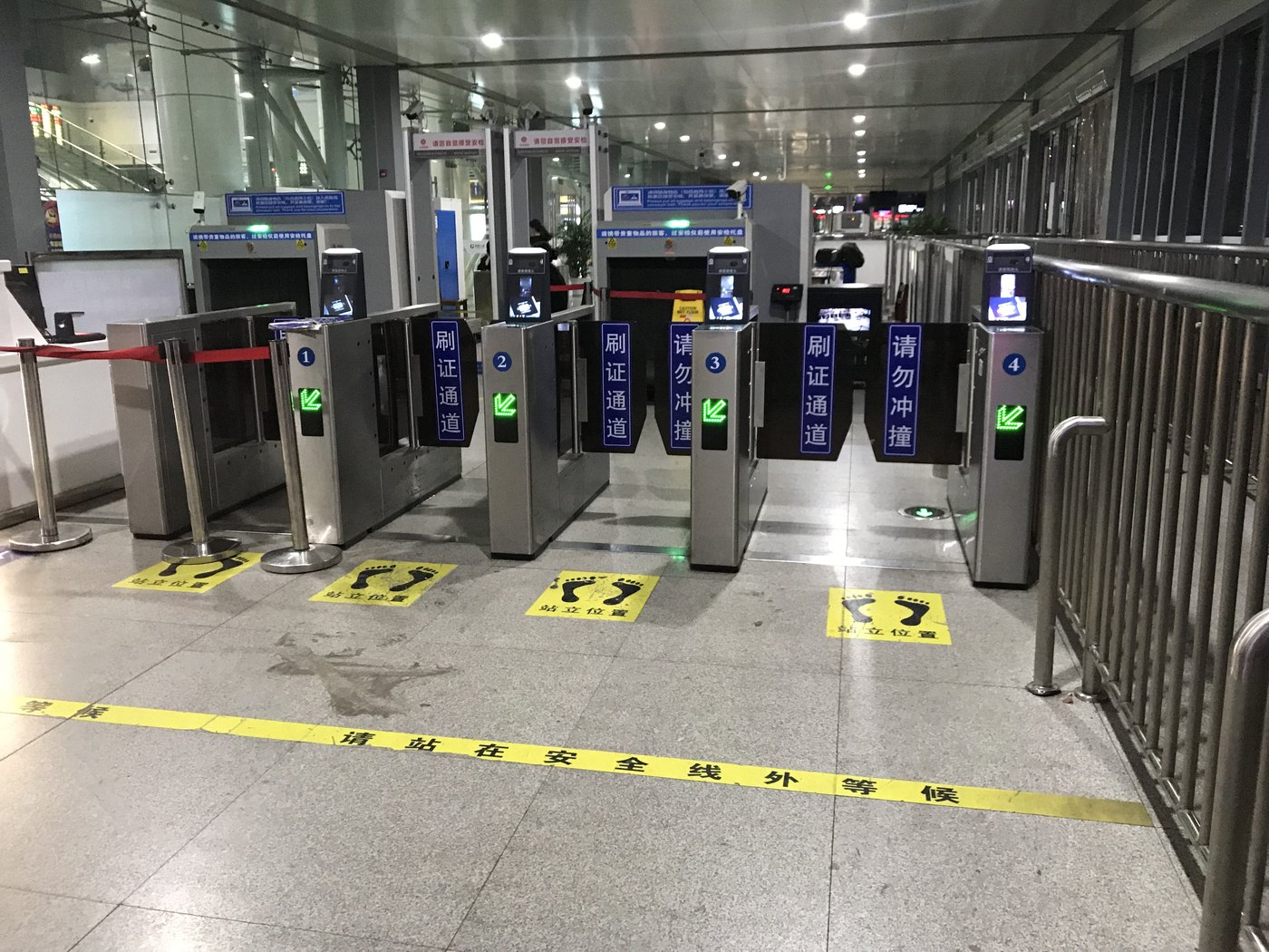 A row of four numbered turnstile gates at a railway station in China, each fitted with a small ID-scan and facial-recognition screen, with blue Chinese-language signage and yellow footprint markers on the floor