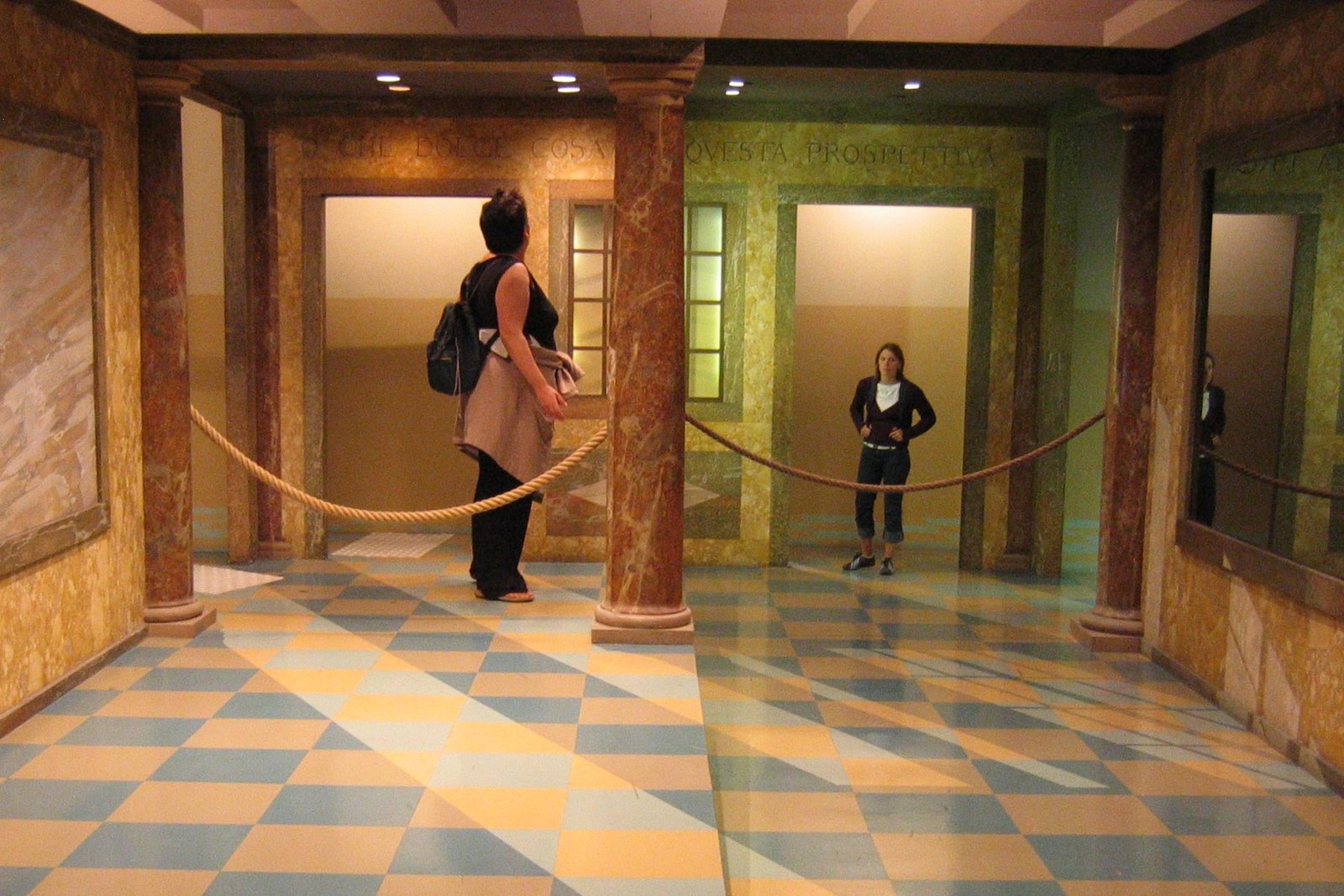 An Ames room exhibit: what looks like an ordinary rectangular room in which one person appears to be a giant and another a dwarf, an illusion produced by the room's secretly trapezoidal shape viewed through a single fixed peephole