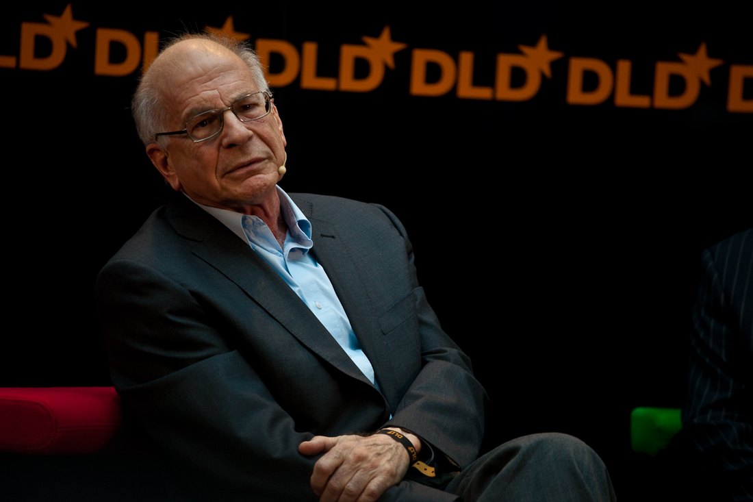 A photograph of the psychologist Daniel Kahneman, an older man, speaking at a public event