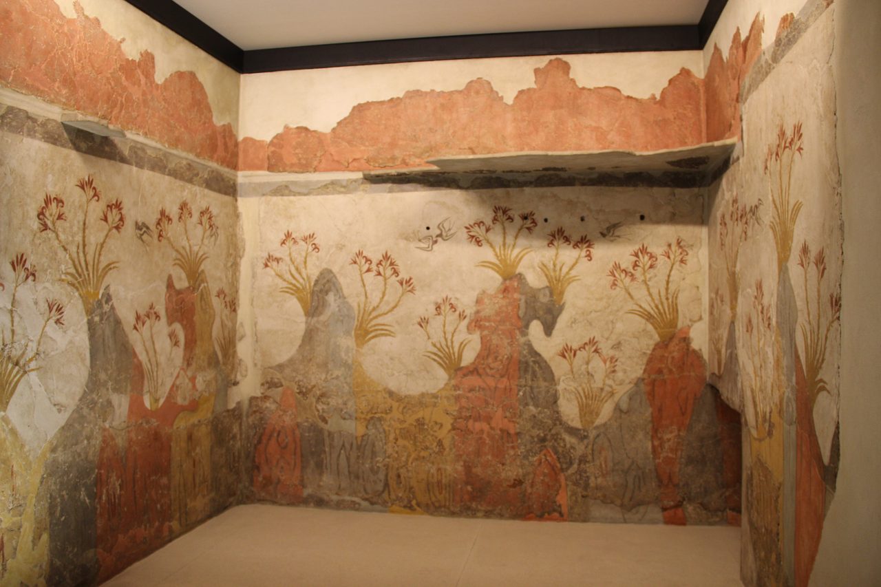 Three walls of a room painted with red lilies rising from undulating rocky ground and dark swallows in flight, the plaster broken and patched, displayed in a gallery with a plain modern floor and ceiling