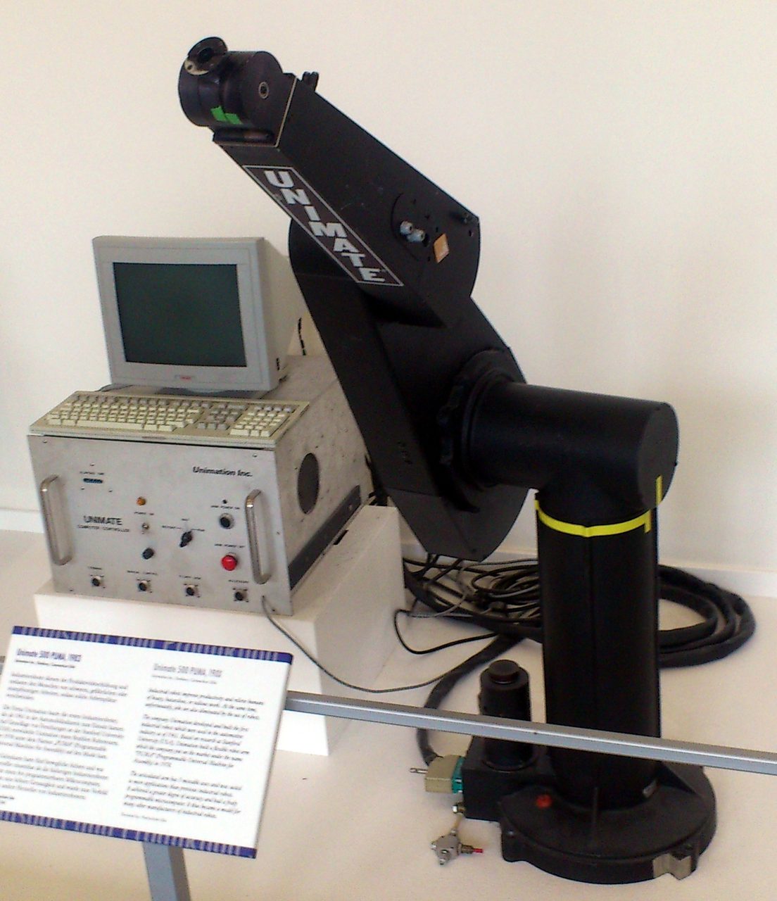 A Unimate 500 PUMA industrial robot arm displayed with its control unit and a computer terminal, an exhibit at the Deutsches Museum in Munich