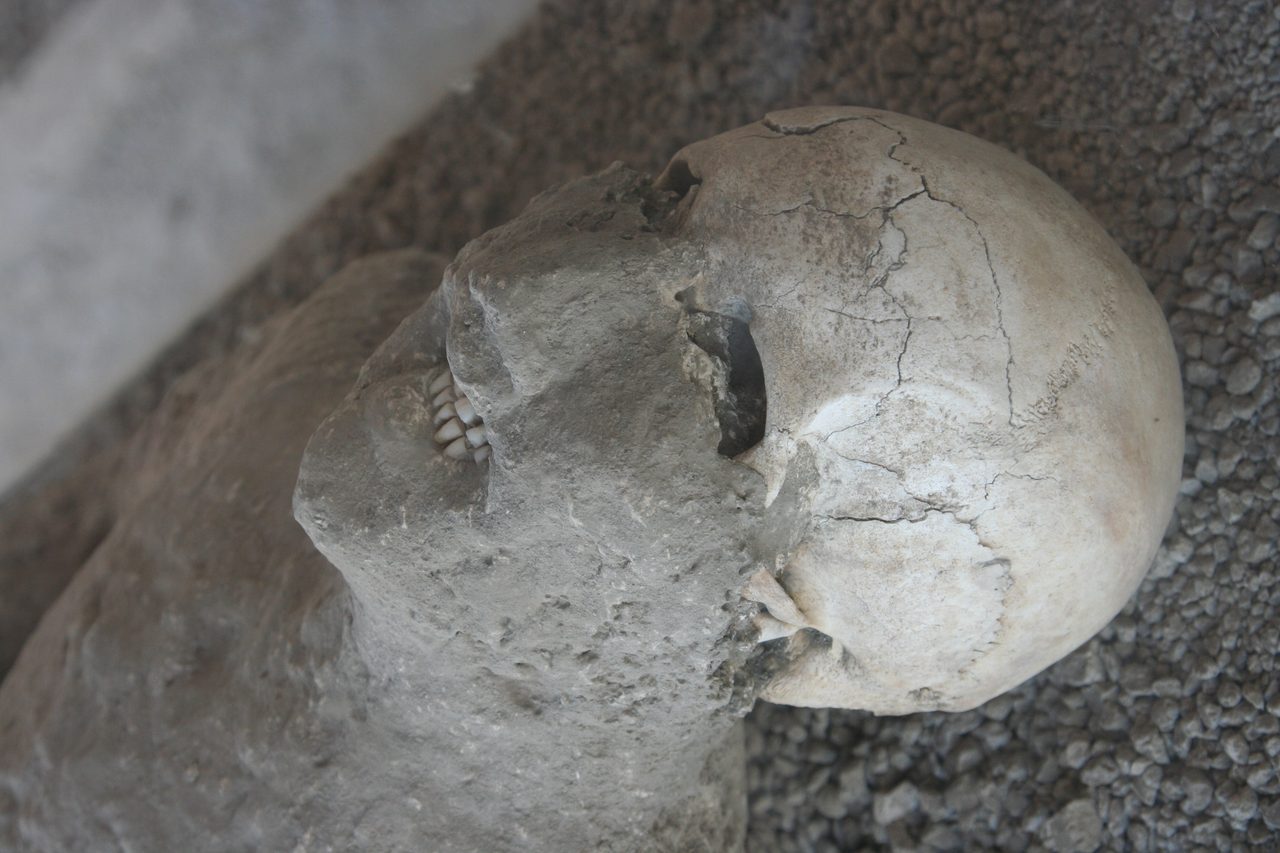 A white plaster cast of a Pompeii eruption victim, preserving the contorted, crouched final position of the body