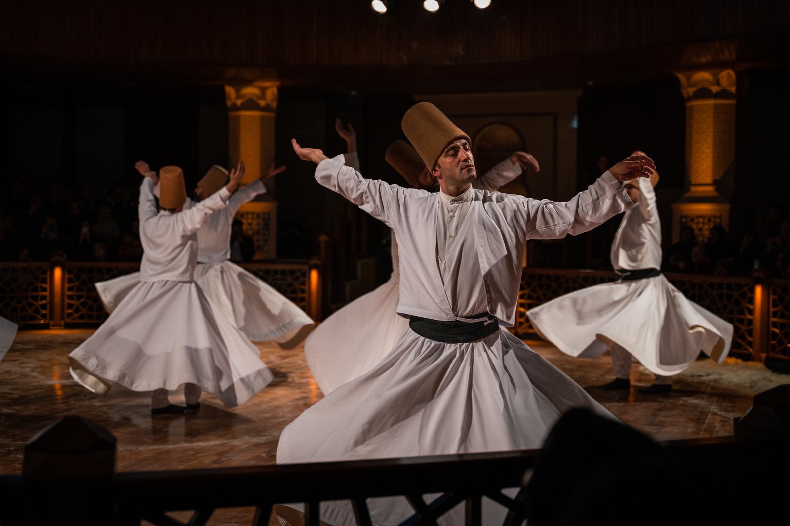 Mevlevi dervishes in white robes and tall camel-hair hats performing the Sema ceremony together in Konya, Turkey, their skirts flared as they turn