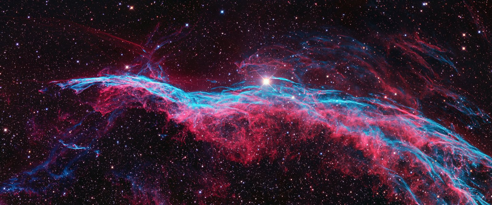 The filamentary red and teal structure of the Veil Nebula against a dense starfield
